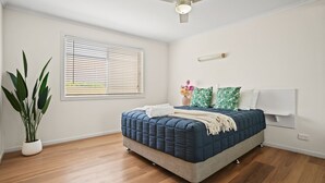 Un dormitorio con una cama, una planta en maceta, una ventana con persianas y un ventilador de techo.
