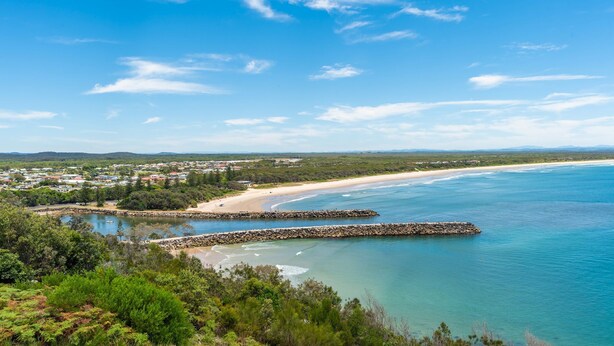 Paisagem costeira com praia, águas azul-claras e uma cidade ao fundo.
