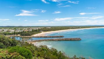 A coastal landscape with a beach, clear blue water, and a town in the background.