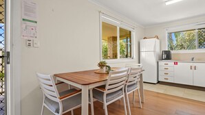 Uma cozinha com mesa e cadeiras de madeira, geladeira e janela com vista para o verde.