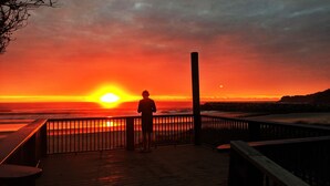 Uma pessoa em um deck de madeira admirando o pôr do sol sobre o oceano.