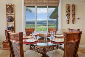 A dining area with a glass table, wicker chairs, and a view of the landscape. - Amazing Ocean, Mountain & Golf Views, Beautiful Ocean Villa (Kamuela)
