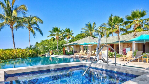 Une piscine entourée de palmiers, avec des chaises longues et des parasols.