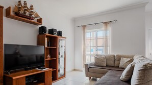 A living room with a flat-screen TV, wooden entertainment unit, and a beige sofa. - 'Alojamento Local Família Coelho' House with Wi-Fi (Quinta do Conde)