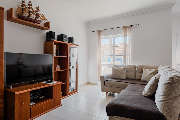 A living room with a flat-screen TV, wooden entertainment unit, and a beige sofa.
