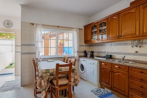 A kitchen with a dining table, chairs, a washing machine, wooden cabinets, and a tiled backsplash.