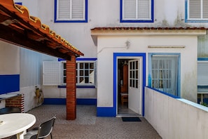 A courtyard with a table and chairs, a door leading to an interior space, and a tiled floor.