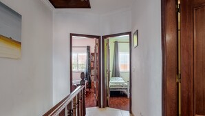 A hallway with a wooden staircase, a bed with a green bedspread, and a view of a balcony. - 'Alojamento Local Família Coelho' House with Wi-Fi (Quinta do Conde)
