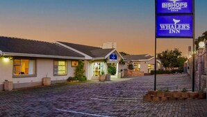 A hotel with a sign for Bishop's Lodge and Whaler's Inn, featuring a paved driveway and a clear sky.