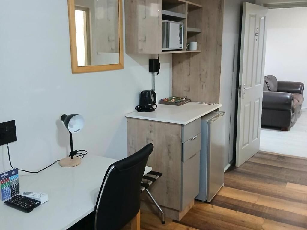 A compact room with a desk, chair, and a small kitchenette area.