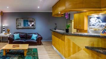Una sala de estar con un sofá de cuero marrón, una mesa de centro de madera y una zona de cocina con encimera y armarios de madera.