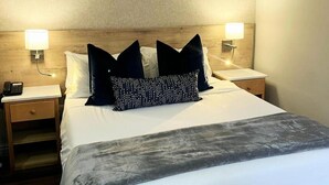 A hotel room with a bed, two bedside tables, a lamp, a phone, and a nightstand.
