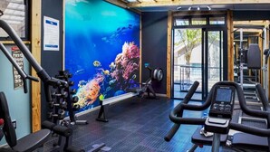 A gym with exercise equipment, a large mural of an underwater scene, and a view of the outdoors.