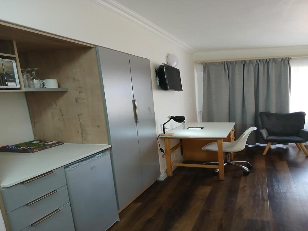 A compact room with a desk, chair, and a television mounted on the wall.