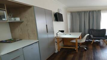 A compact room with a desk, chair, and a television mounted on the wall.