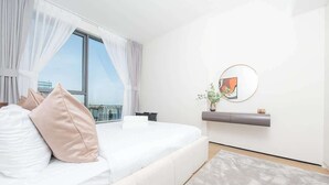 Une chambre moderne avec un grand lit, une vue sur la ville, une œuvre d’art accrochée au mur et une petite plante posée sur la table de chevet.