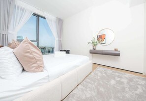 Ein modernes Schlafzimmer mit einem großen Bett, Blick auf die Stadt, einem Wandbild und einer kleinen Pflanze auf dem Nachttisch.