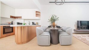 Une cuisine moderne dotée d’un îlot central, un coin repas avec deux canapés gris et un téléviseur à écran plat situé à droite.