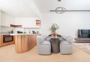 Eine moderne Küche mit einer zentralen Kochinsel, einem Essbereich mit zwei grauen Sofas und einem Flachbildfernseher auf der rechten Seite.