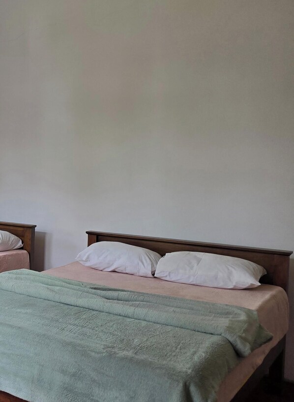 Un lit simple avec une couverture verte et deux oreillers, une tête de lit en bois et un mur uni.