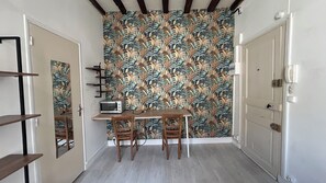 Un couloir étroit avec une table en bois et deux chaises, un four à micro-ondes et un papier peint à motifs floraux.