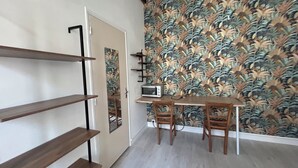A room with a wooden desk, a microwave, and a patterned wall. Shelves are mounted on the wall. - Beautiful Studio T1 in Vieux tours (tours)
