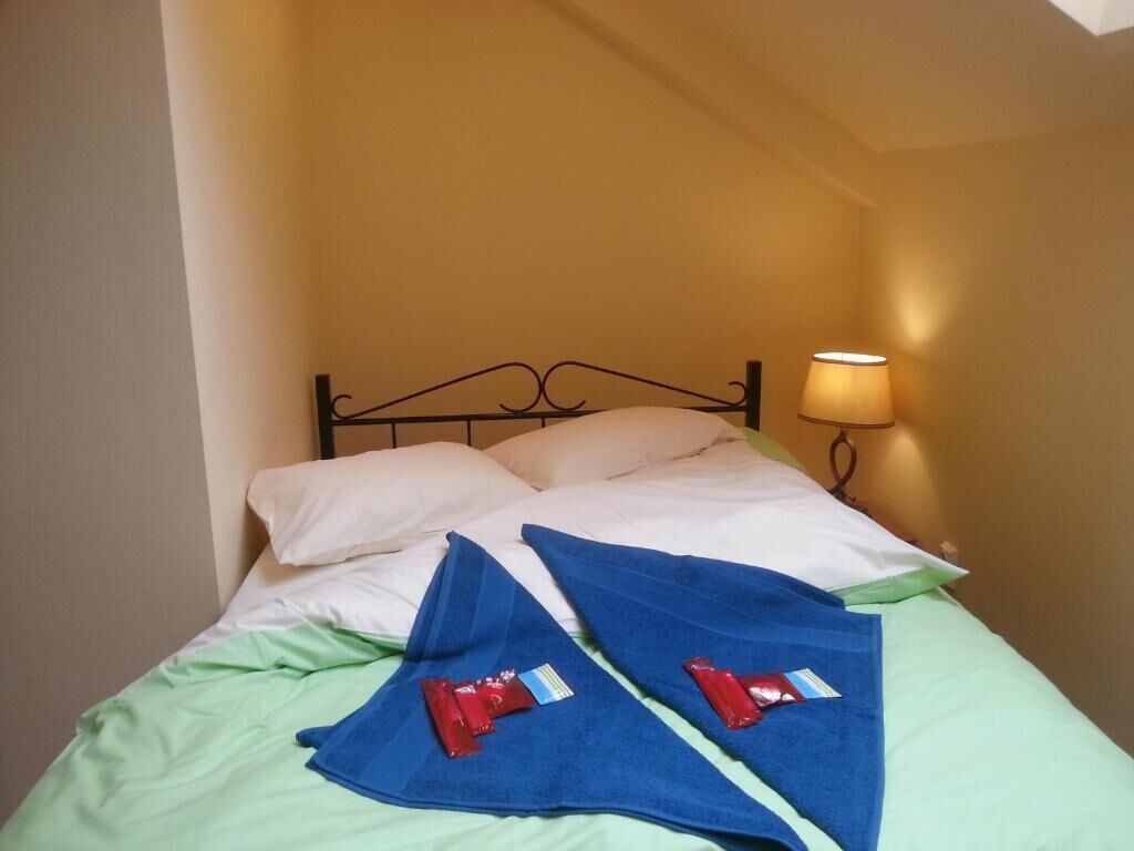 A bed with a metal frame, white pillows, green sheets, and two red towels.
