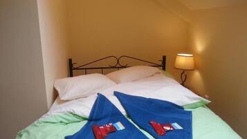 A bed with a metal frame, white pillows, green sheets, and two red towels.