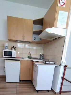 Een compacte keuken met houten kastjes, een magnetron, een spoelbak en een kleine koelkast.