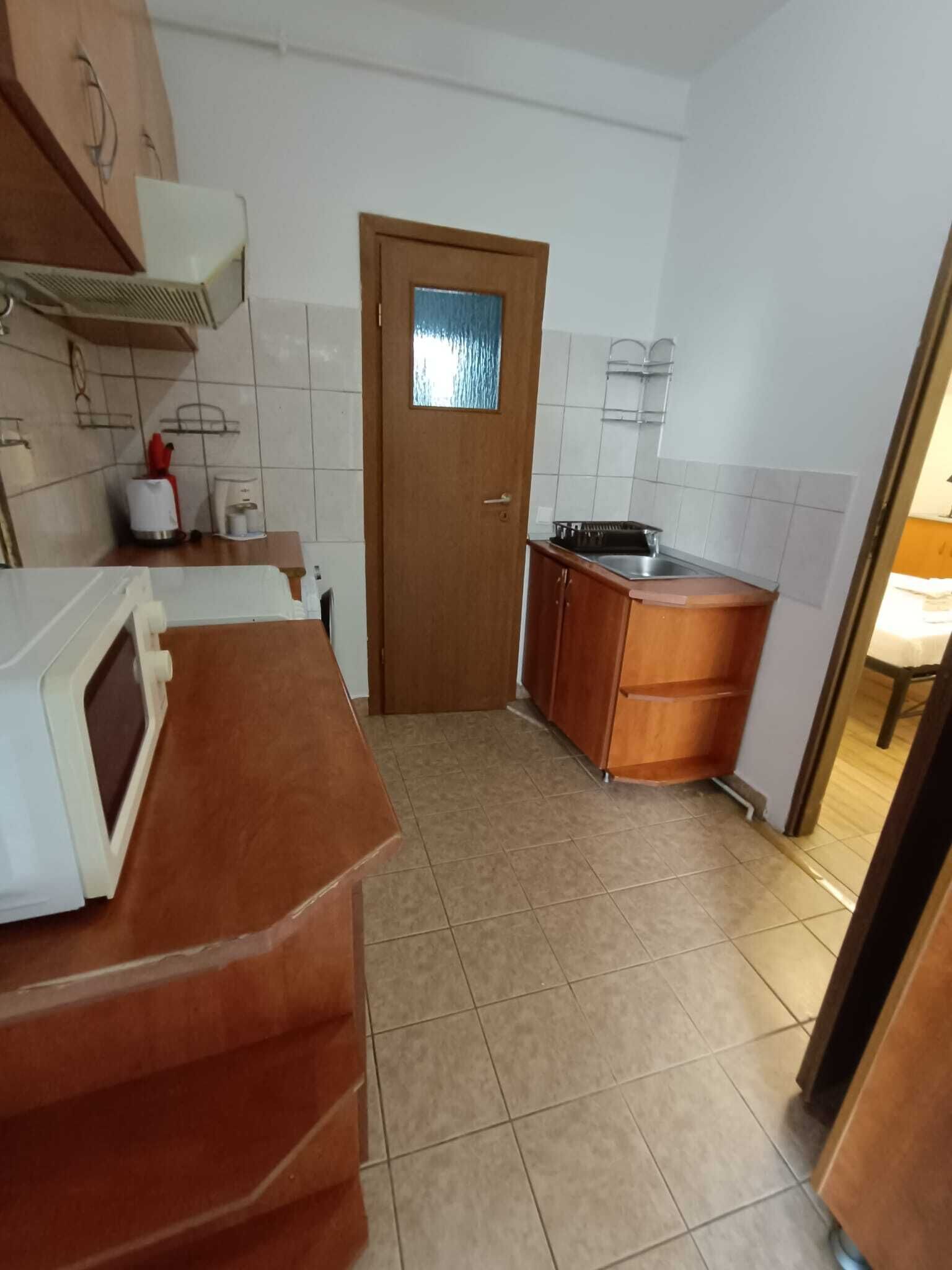 A kitchen with a wooden door, white tiled walls, and a countertop with a microwave.