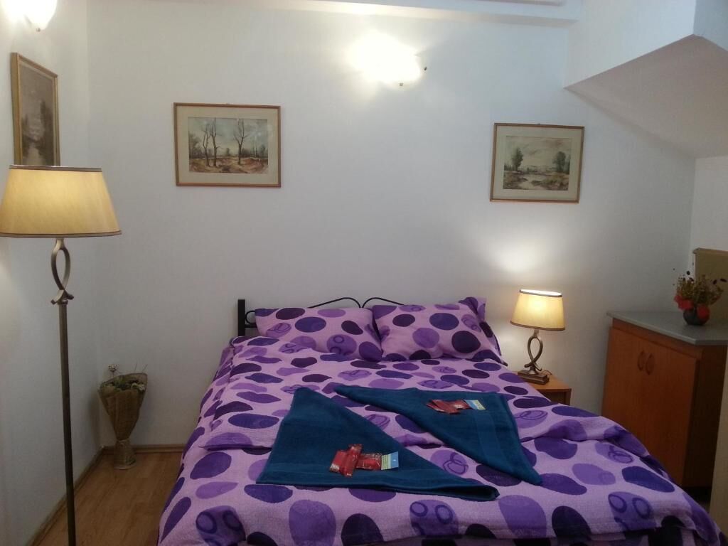 A bedroom with a bed, two wall-mounted lamps, a nightstand, a wooden cabinet, and two framed pictures on the wall.