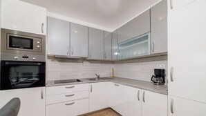 Una cocina moderna con armarios blancos, horno empotrado, microondas y cafetera.