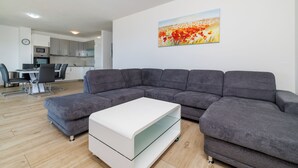 Una sala de estar moderna con un sofá modular, una mesa de centro de vidrio y un comedor al fondo.