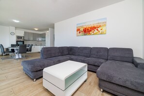 Ein modernes Wohnzimmer mit einer Eckcouch, einem Couchtisch mit Glasplatte und einem Essbereich im Hintergrund.