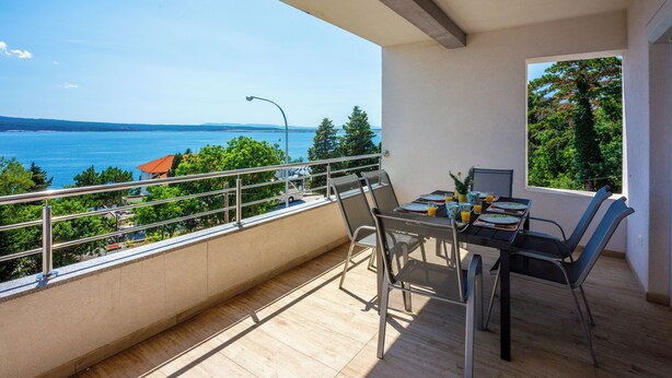 Un balcón con una mesa y sillas de comedor, con vistas a una masa de agua y follaje.