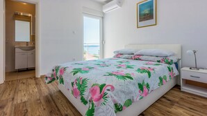 Un dormitorio con cama, mesita de noche, lámpara de noche, ventana con vistas y baño con lavabo y espejo.