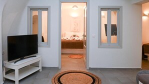 A room with a television on a stand, a doorway leading to a bedroom, and a patterned rug on the floor. - mati cave villas (Santorini)