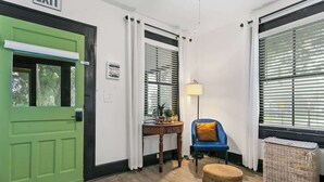 A room with a green door, a blue chair, a small table with a lamp, and a wicker basket. - Cozy Bungalow Near Shops-st Augustine (St. Augustine)