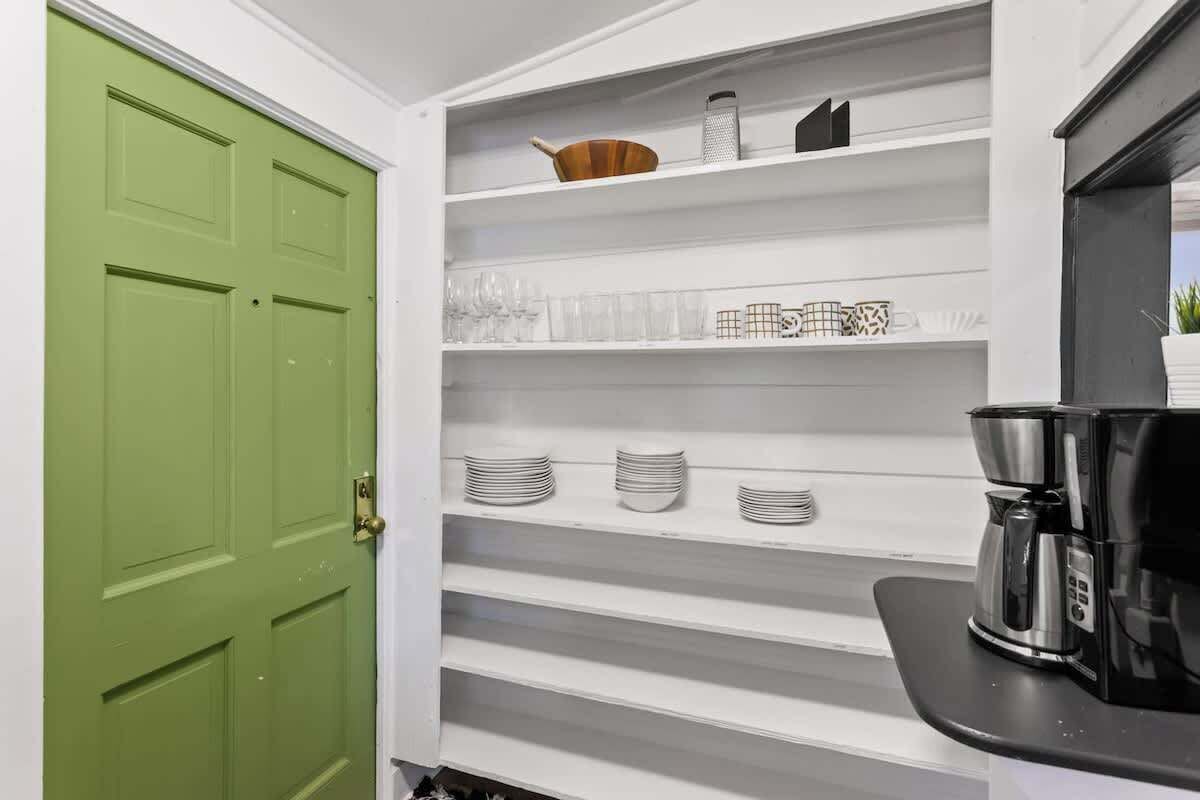 A kitchen with white shelves, a green door, and a coffee maker.