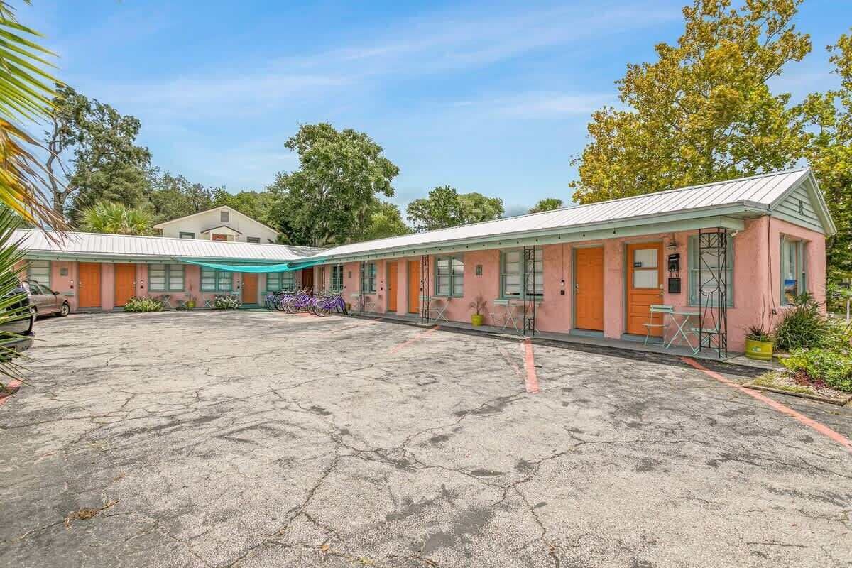 A row of pink motel buildings with a large parking lot in front.