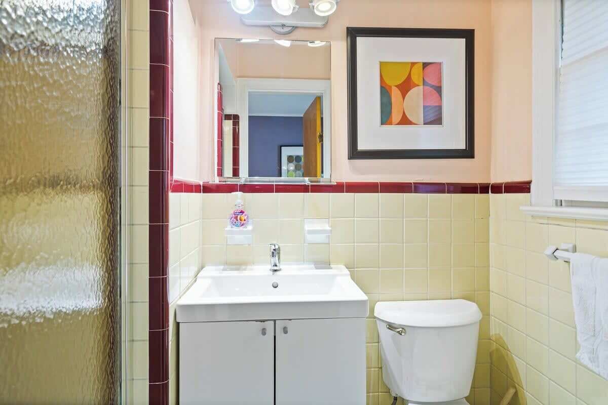 Une salle de bain avec un lavabo blanc, des toilettes, un miroir et un tableau abstrait encadré accroché au mur.