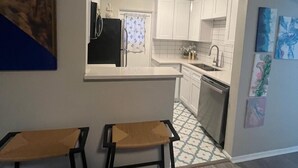A compact kitchen with white cabinets, a black refrigerator, and a dishwasher. There are two stools and a small table. - Winter Park Spacious Unit - 118 (Winter Park)