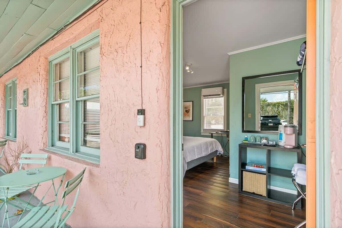 A room with a bed, a small table, and a chair, a window, and a mirror.