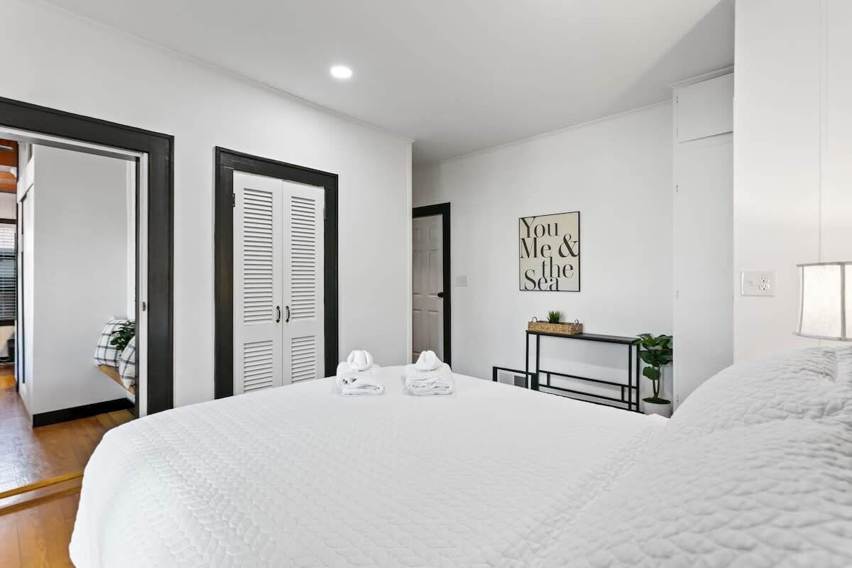 A bedroom with a large bed, a bedside table with a lamp, and a framed quote on the wall.