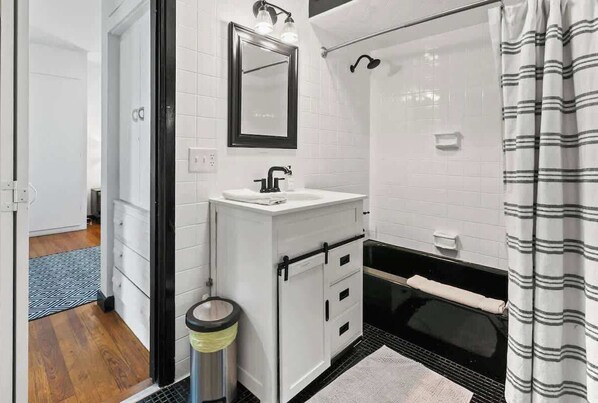 A bathroom with a white sink, black faucet, and a mirror above it. There is a shower curtain with a striped pattern. - Unique Pet Friendly Bungalow in St Augustine (St. Augustine)