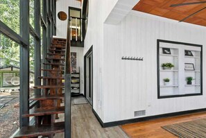 A modern interior with a wooden staircase, white walls, and a black-framed window with shelves. - Unique Pet Friendly Bungalow in St Augustine (St. Augustine)