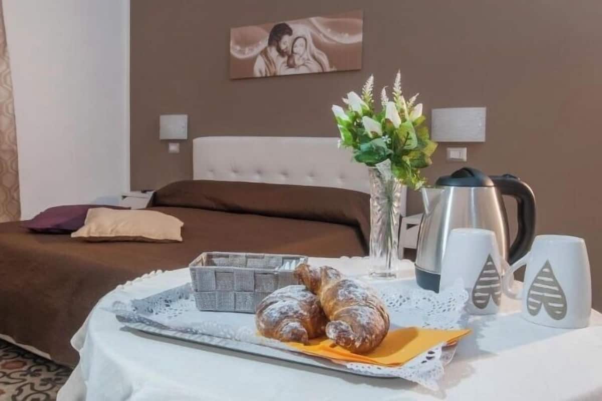 A hotel room with a bed, a vase with flowers, a tray with pastries, and a coffee maker.