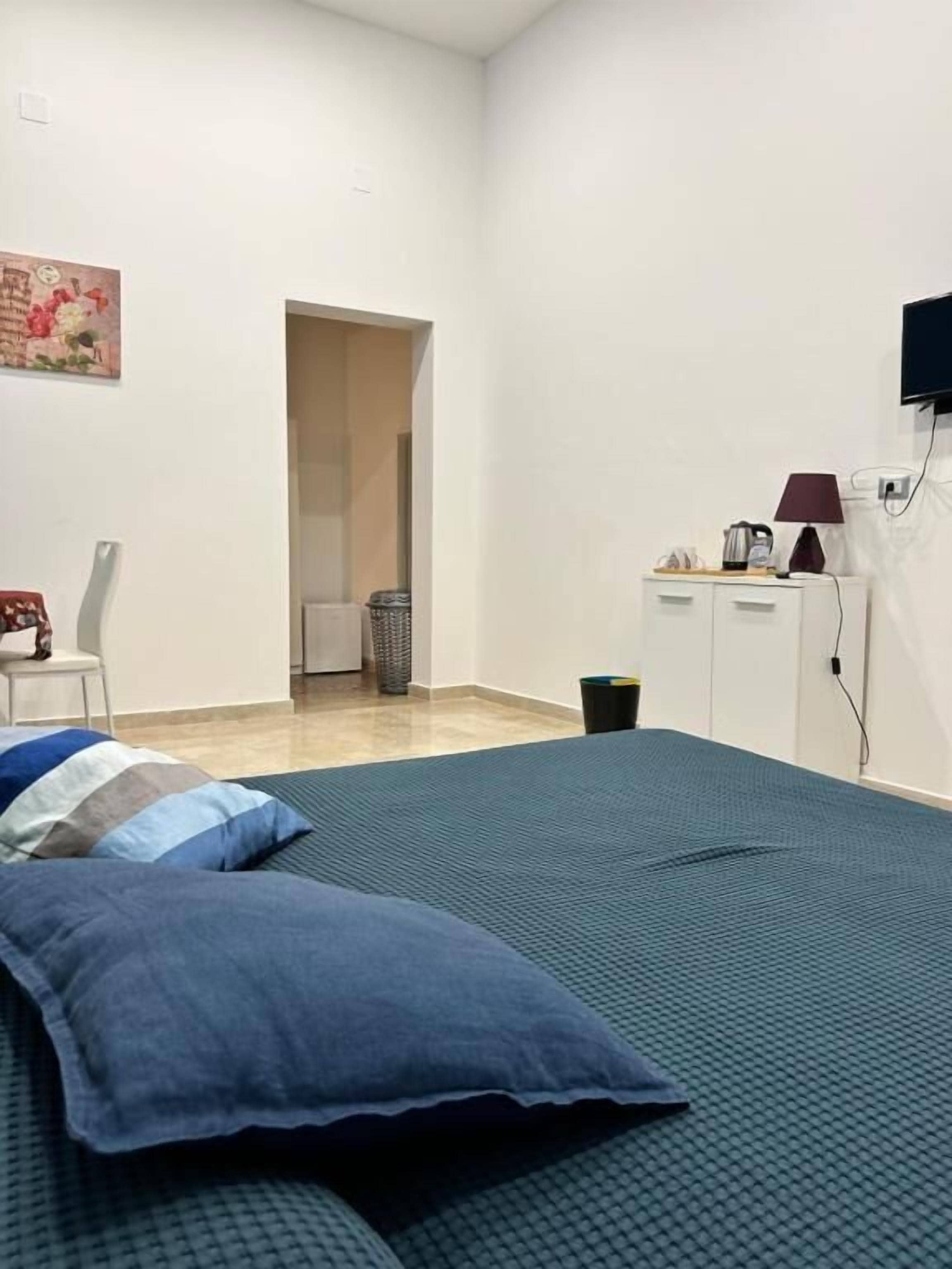 Un dormitorio con una cama, un escritorio, una silla, un televisor y una puerta que da a otra habitación.