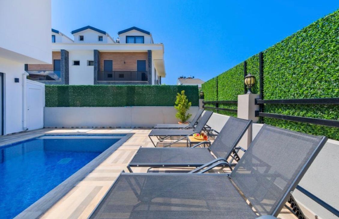Une piscine avec des chaises longues, une haie verdoyante et un bâtiment moderne en arrière-plan.