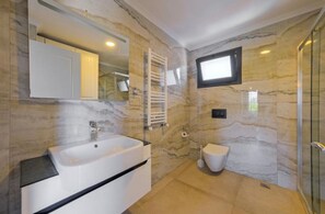 A bathroom with a marble wall, a sink, a toilet, and a shower. - FETHİYE VİLLA MELEK (Muğla)
